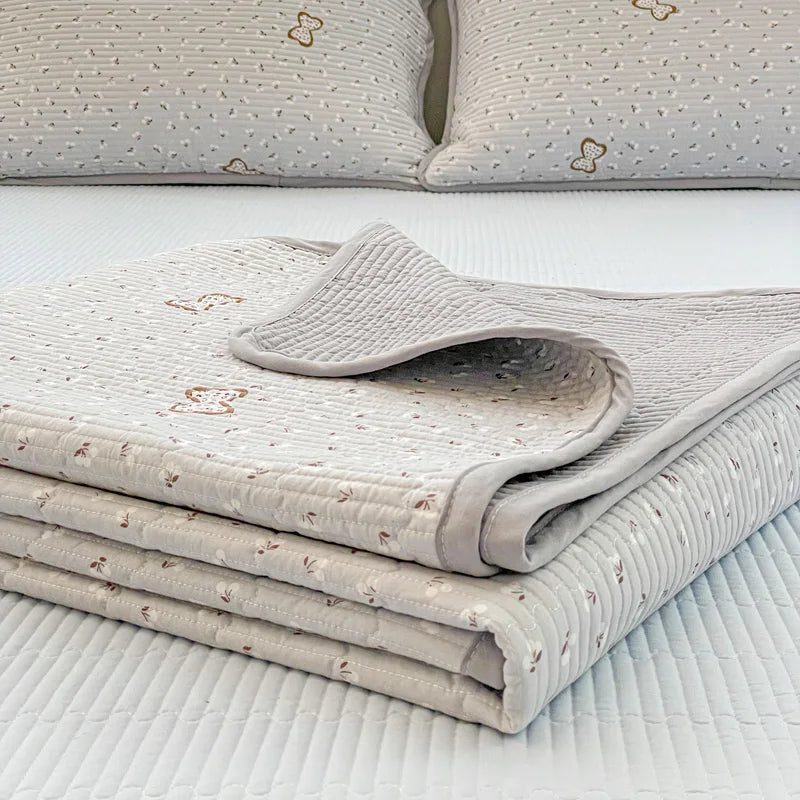 A stack of light beige floral quilted polyester coverlets and pillows on a white bed.