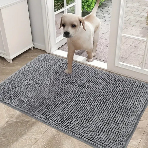 A light-colored puppy stands on a gray, fluffy chenille door mat placed in a doorway.