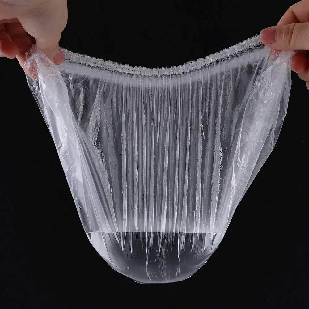 A clear plastic disposable shower cap with an elastic edge is being held by a hand.