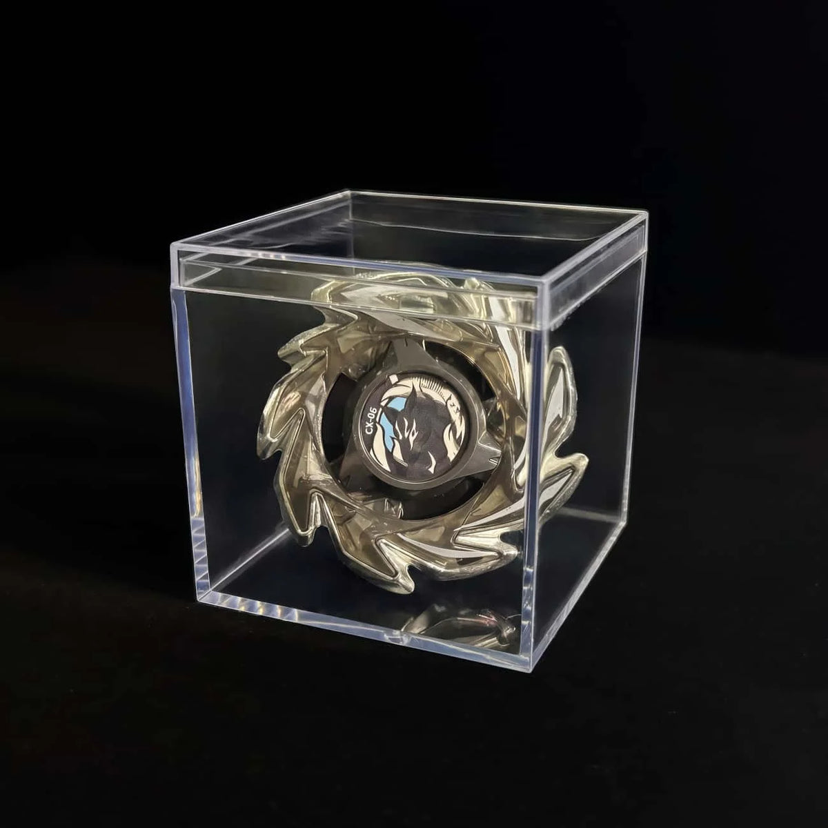A silver metal spinning top with a launcher is displayed inside a clear acrylic box.