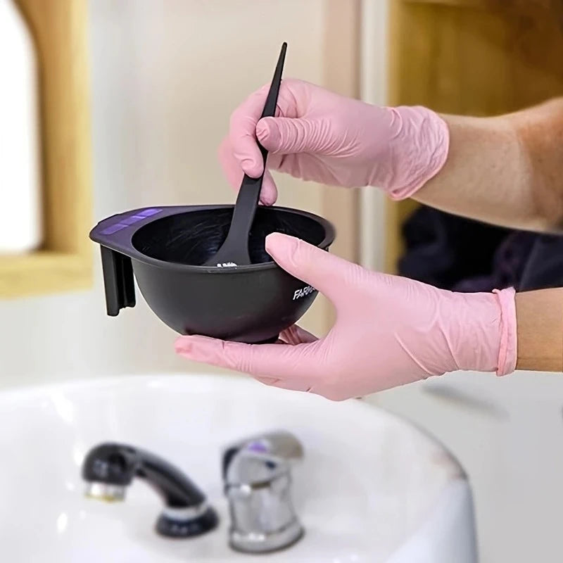 A hand wearing a pink nitrile glove is using a black silicone bowl to clean a faucet.