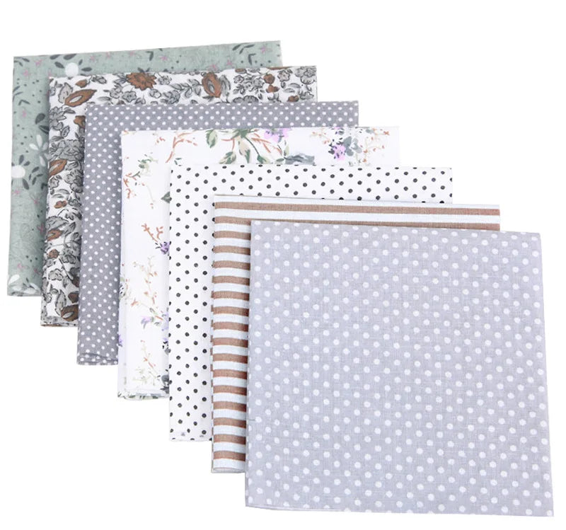 A bundle of cotton fabric squares featuring various floral and dot patterns in muted greens, grays, and neutrals.