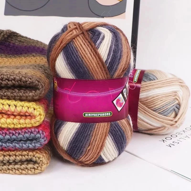 A ball of gradient dyed wool blend yarn in shades of brown, purple, and gray is shown next to a skein on a white background.