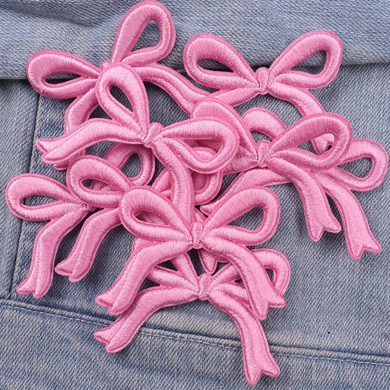 Pink felt cartoon bow embroidered iron-on patches scattered on a denim fabric.