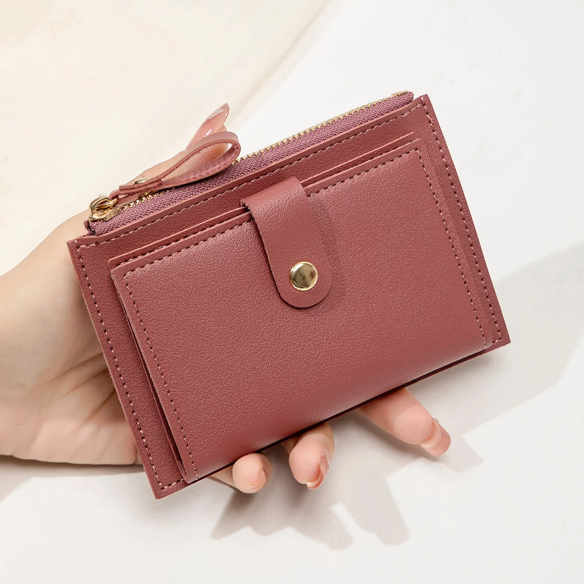 A close-up of a mauve pink women's slim PU leather card holder wallet being held in a hand.