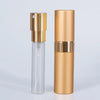 A tall, cylindrical aluminum perfume atomizer with a clear glass bottle and a gold-colored cap and body.