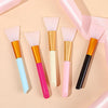A collection of silicone facial mask brushes in various colors including pink, orange, blue, and black, displayed on a light 