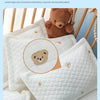 White quilted baby pillow with a bear design and a teddy bear toy in the background.