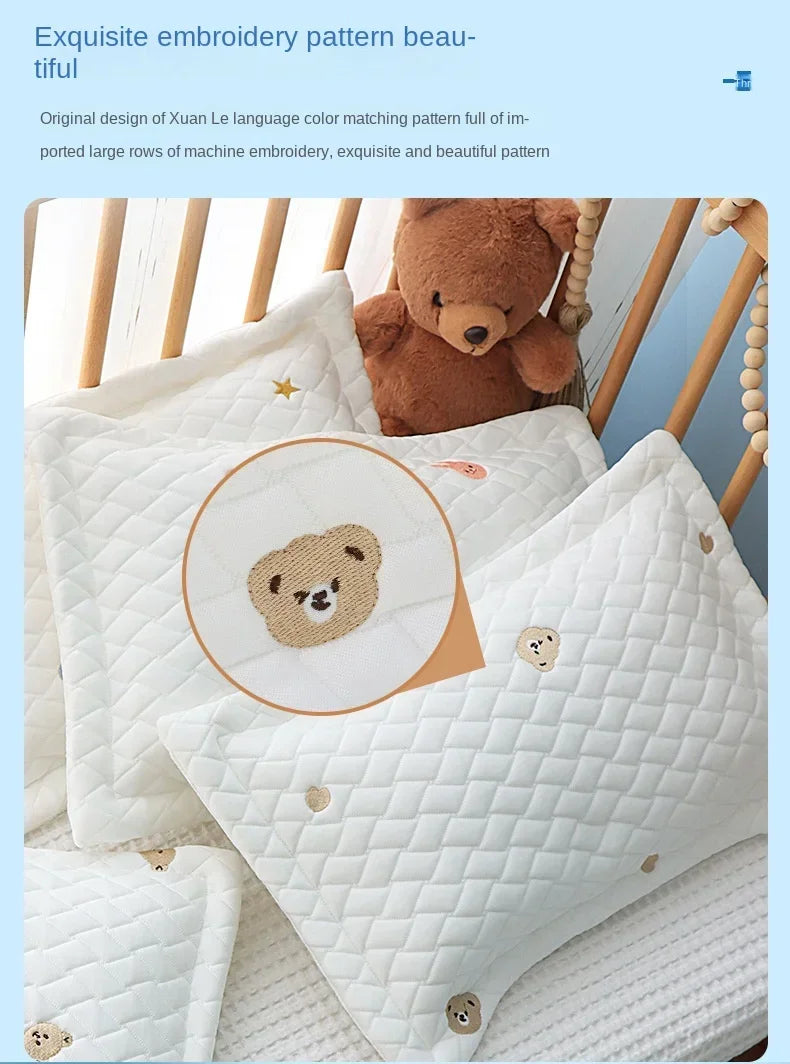 White quilted baby pillow with a bear design and a teddy bear toy in the background.