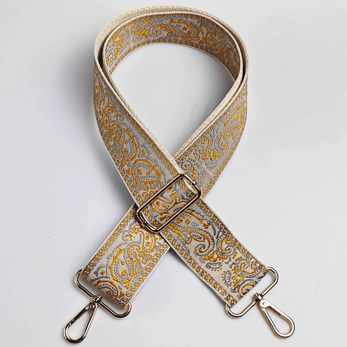 A beige and gold paisley jacquard bag strap with a silver buckle and metal hardware.