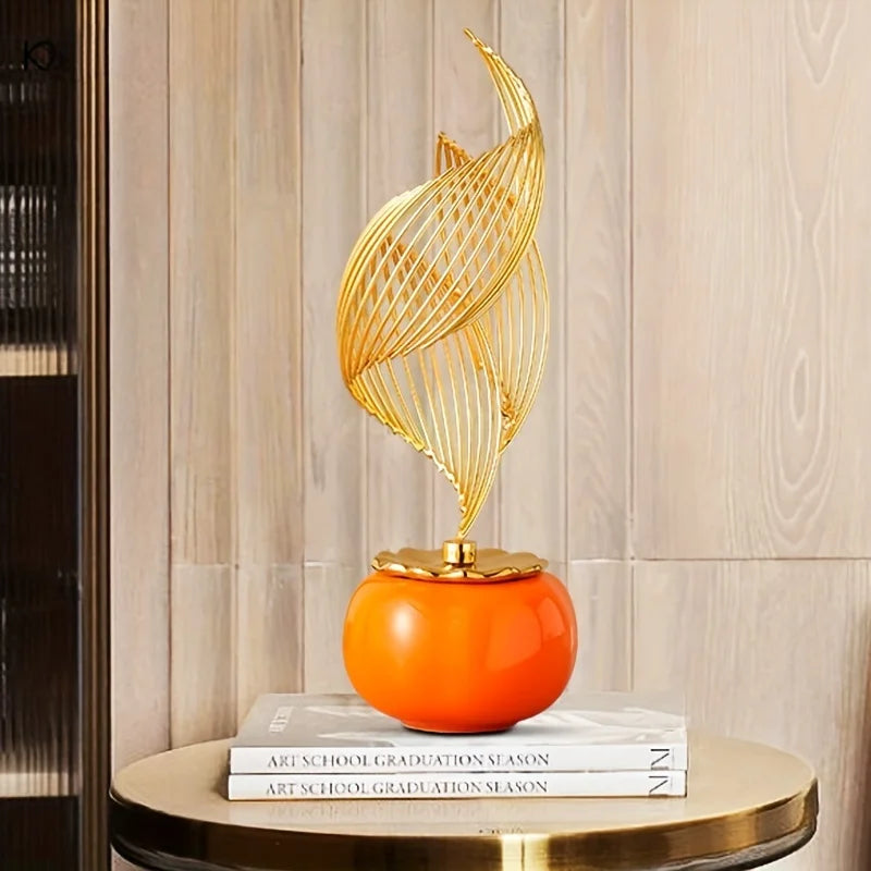 A golden, leaf-like ceramic sculpture sits on an orange sphere atop a stack of books.