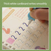A hand writes smoothly on a white cardboard handwriting practice book with numbers and letters.