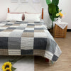 A patchwork cotton bedspread featuring a gray, black, and white checkered pattern on a bed.
