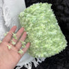 A hand is holding a ball of light green variegated cotton blend yarn for knitting and crochet.