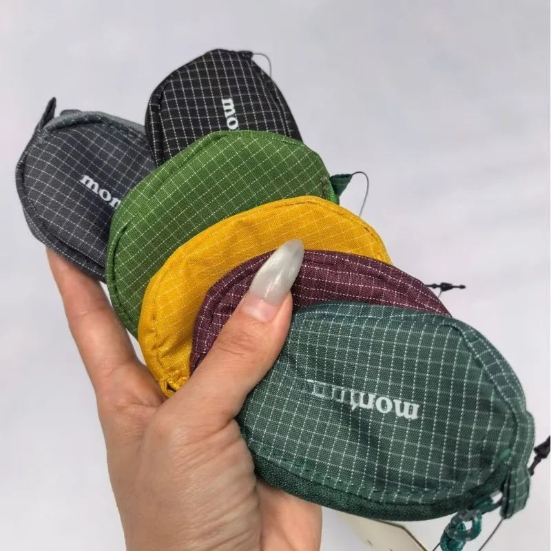 Une main tient plusieurs pochettes en nylon à écouteurs et clés, dans différentes nuances de vert, jaune et gris.