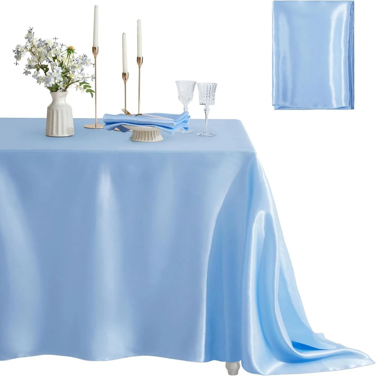 A light blue satin tablecloth set for dining featuring a floral centerpiece, candles, and glassware.