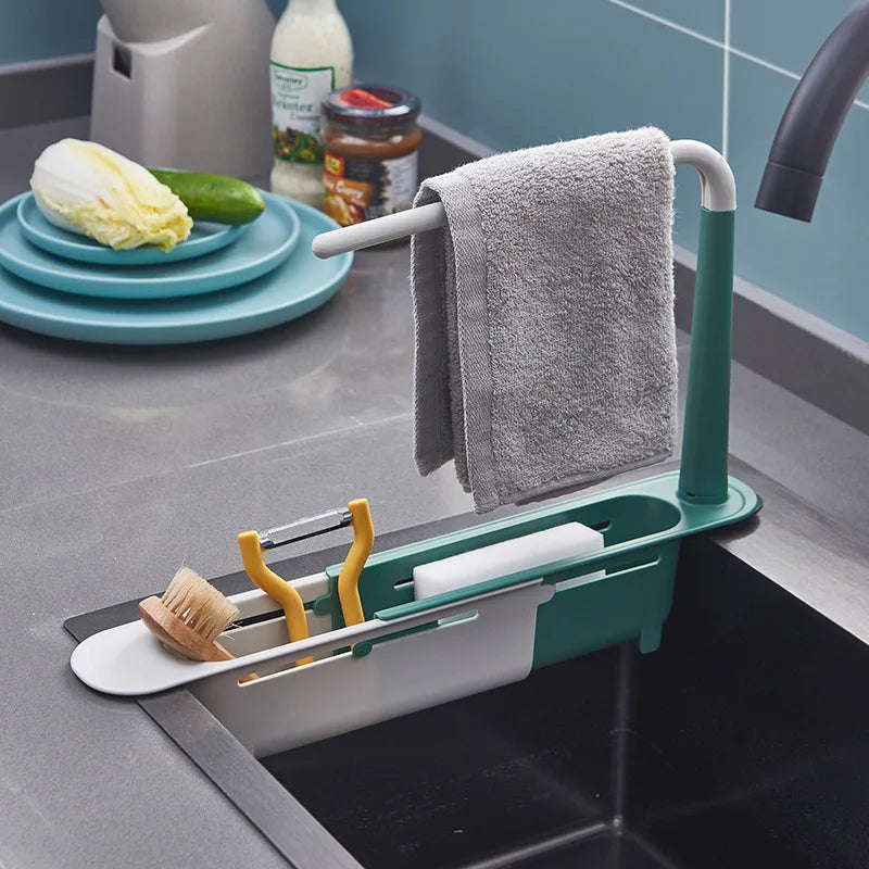 A green adjustable sink sponge holder with a towel rack and drainer basket sits on a kitchen sink.