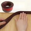 A roll of brown door draft stopper material next to a hand demonstrating the flexible, self-adhesive under-door seal.