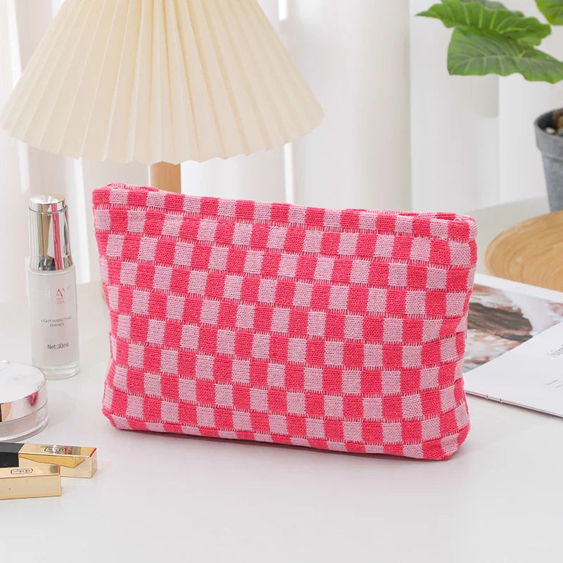 A pink and white checkered plaid makeup bag with a zipper lying on a white surface.