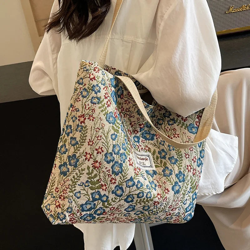 A light floral patterned corduroy tote bag carried by a person wearing a white blouse.