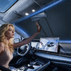 A woman is adjusting a foldable car windshield sunshade in the interior of a car.