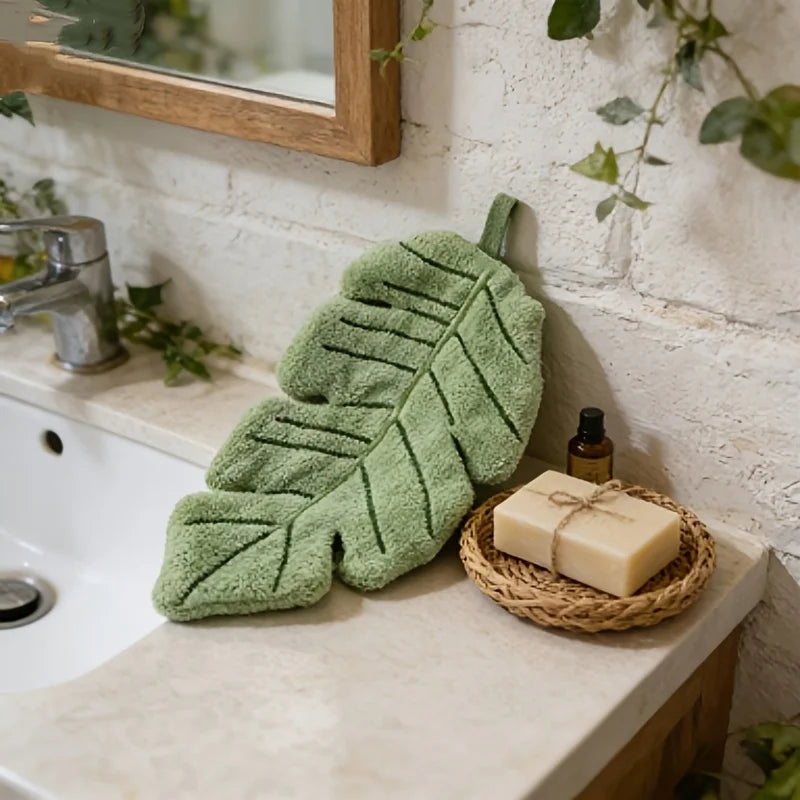 A green banana leaf absorbent hand towel resting on a white countertop next to a bar of soap.