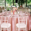 A round table set for an event featuring a pink satin tablecloth, white chairs, and floral centerpieces.
