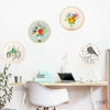 A collection of circular embroidery pieces featuring floral designs on a white wall above a wooden desk.