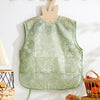 A light green waterproof baby feeding bib with a floral pattern hanging on a white wall.