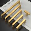 Fünf goldfarbene Edelstahl-Schrankgriffe diagonal auf einer weißen Fläche angeordnet.