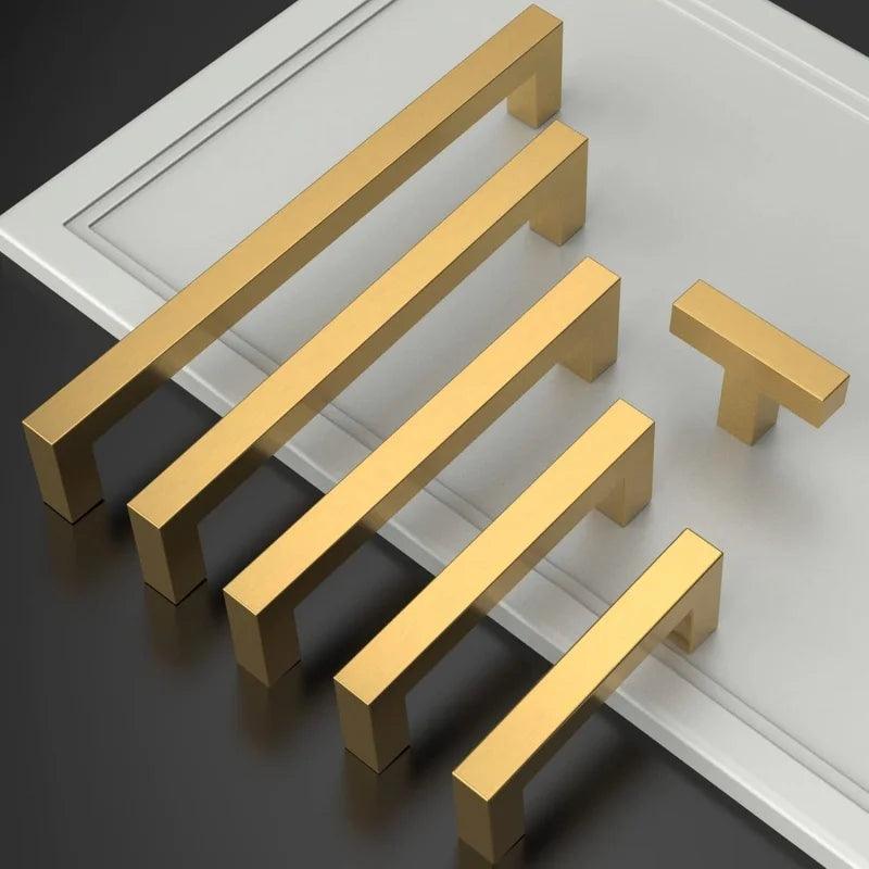 Fünf goldfarbene Edelstahl-Schrankgriffe diagonal auf einer weißen Fläche angeordnet.