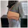 A woman is holding a tan vintage leather crossbody bag with a flap closure against a light background.