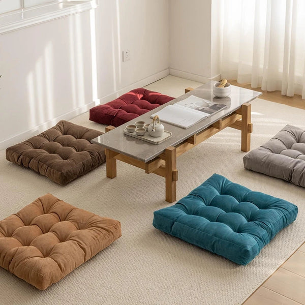 A collection of tufted floor seating cushions in shades of brown, gray, and teal arranged in a bright room.