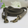 A brown canvas adjustable shoulder strap with brass hardware is displayed on a white surface.
