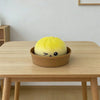 A yellow squishy stress relief toy shaped like a face is placed in a brown bowl on a wooden table.