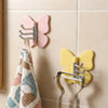 Un juego de ganchos decorativos de mariposa giratoria en rosa y amarillo contra un fondo de azulejos.