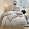 A light gray duvet cover set with matching pillows on a bed, next to a window and a lamp.