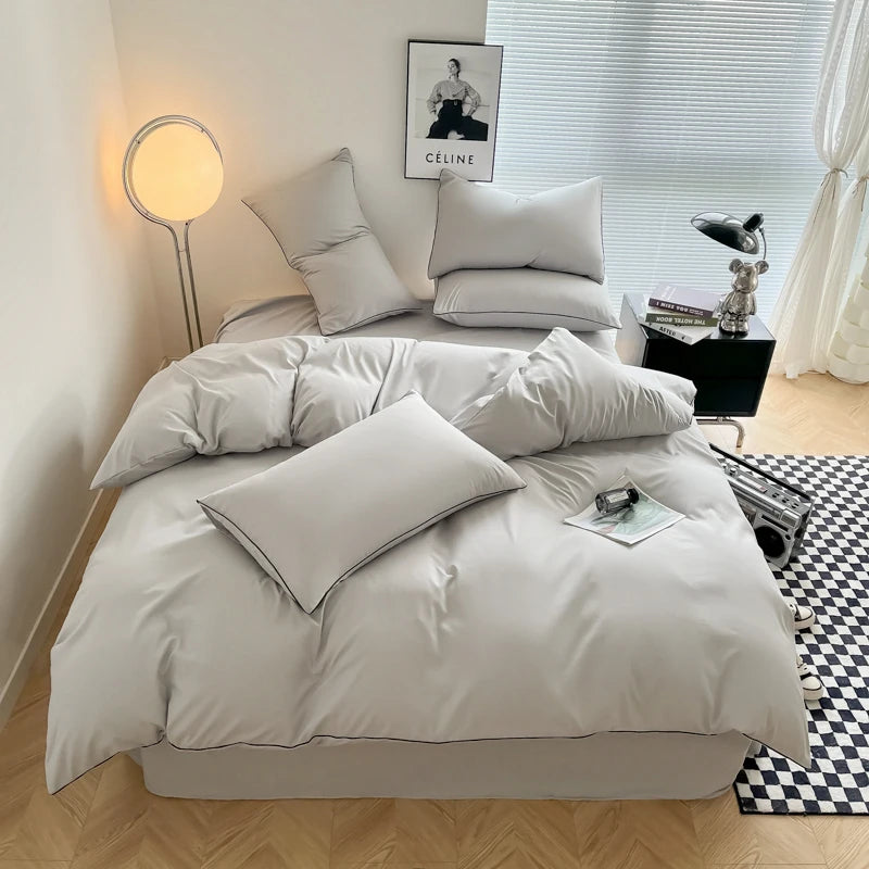 A light gray duvet cover set with matching pillows on a bed, next to a window and a lamp.