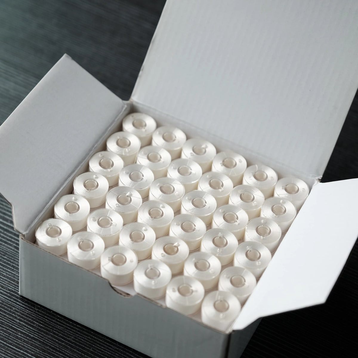 A white box filled with numerous prewound bobbins for home embroidery machines.