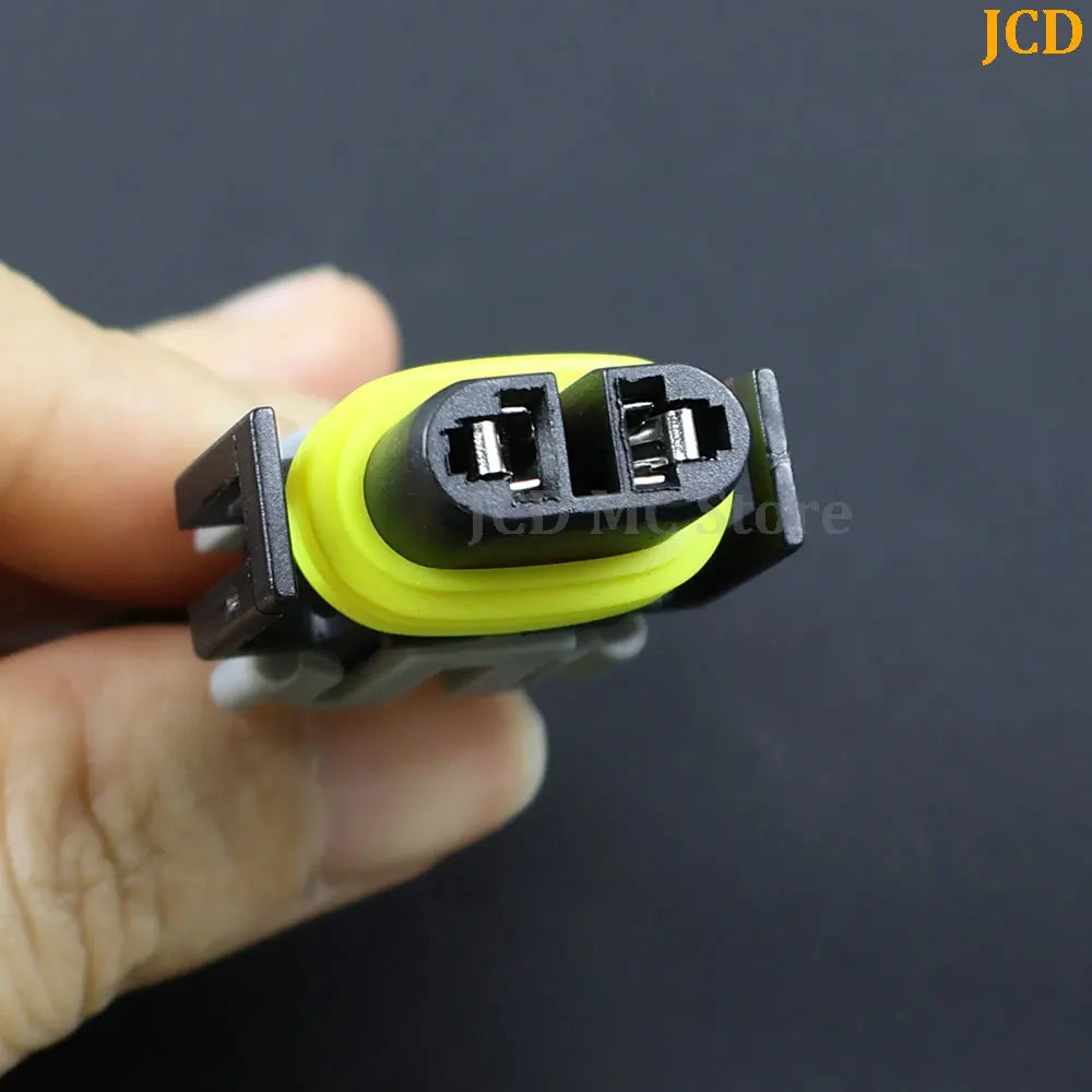 A hand holds an H8/H11 headlight adapter wiring harness with a yellow and black connector.