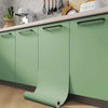 A set of matte green vinyl film rolls for furniture and wall renovation displayed on a kitchen cabinet.