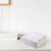 A white, rectangular storage box for trading cards is placed on a white surface next to some stacked white cards.