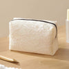 A rectangular white lace mesh makeup bag is shown on a wooden surface with a gold applicator nearby.