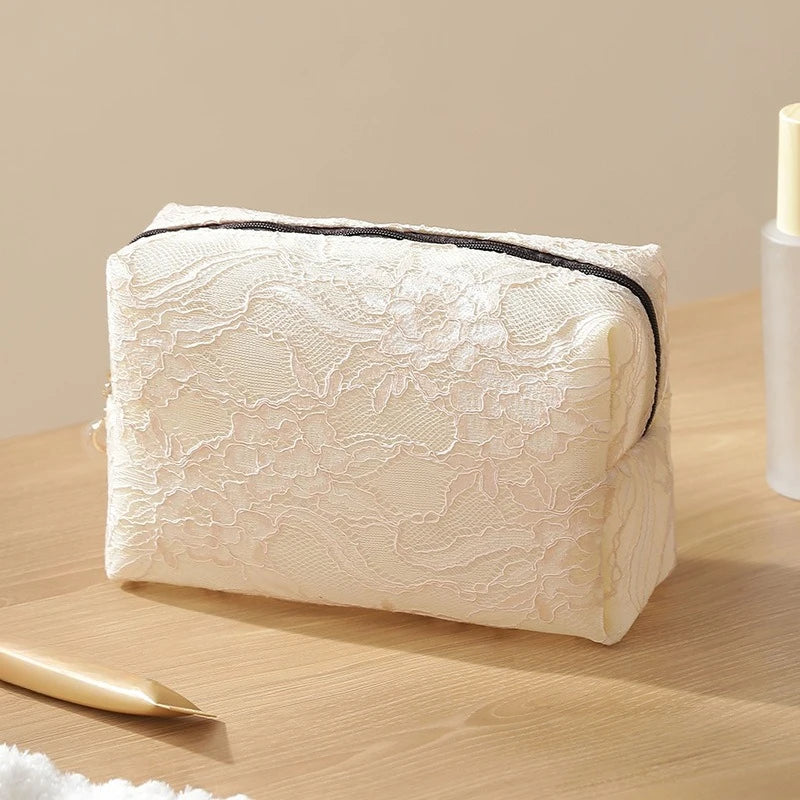 A rectangular white lace mesh makeup bag is shown on a wooden surface with a gold applicator nearby.