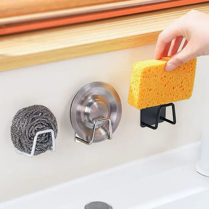 A hand is holding a yellow sponge over a stainless steel suction cup holder mounted on a white sink surface.