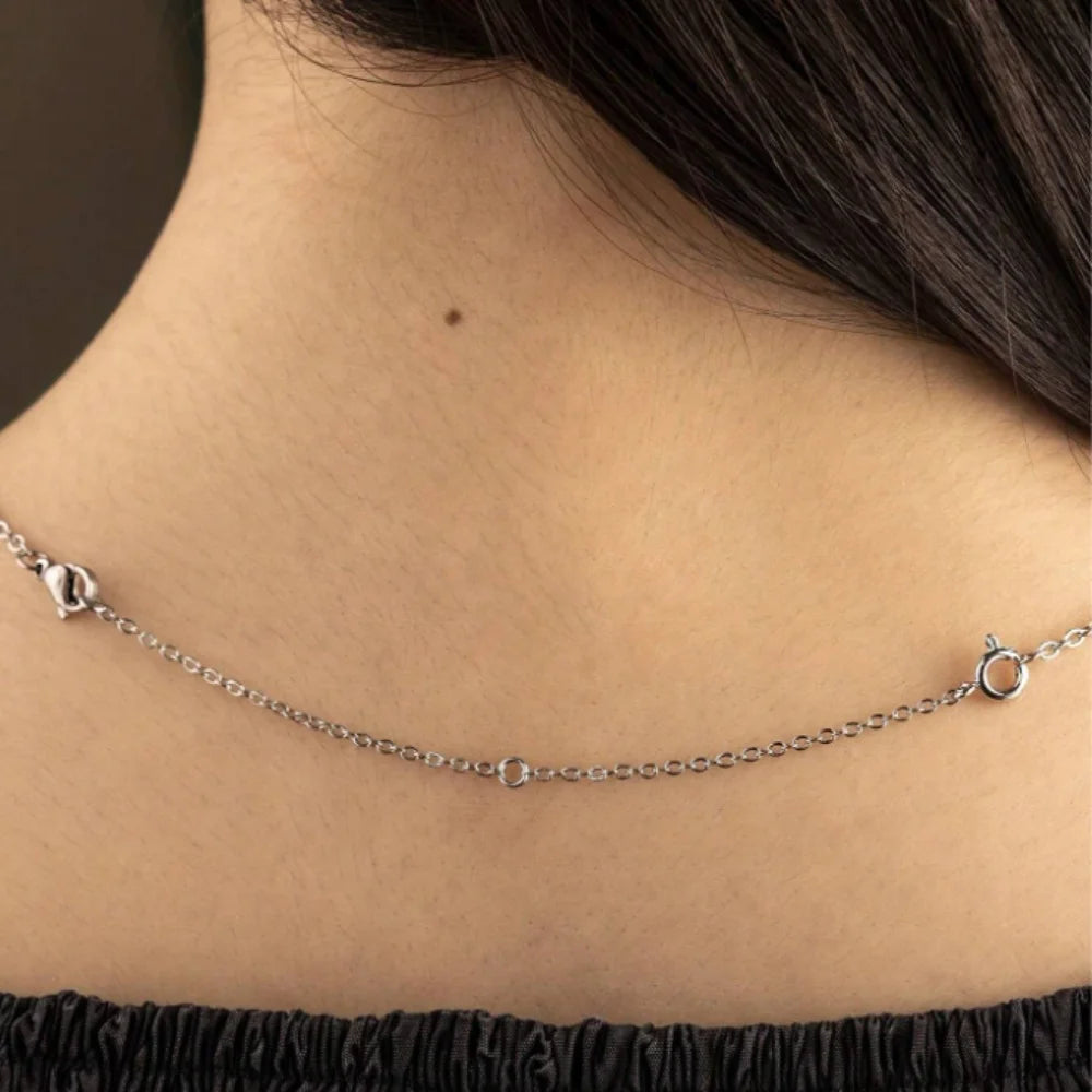 A close-up of a silver gold-plated necklace extender chain with a lobster clasp worn around a woman's neck.