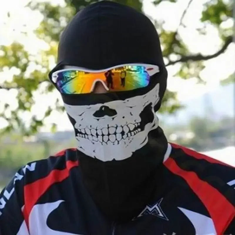 A person wearing a black balaclava with a white skull print and mirrored sunglasses outdoors.