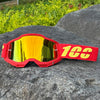 Red motocross goggles with yellow mirrored lenses resting on a dark gray rock.