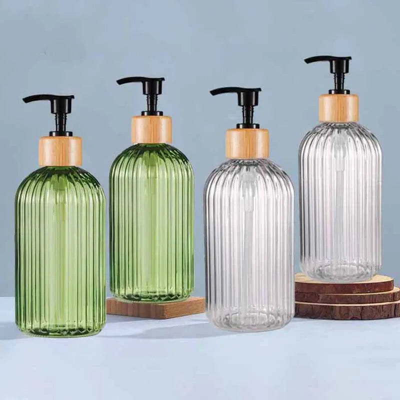 A set of four refillable soap dispensers in varying shades of green and clear glass with black pump tops on a light blue surf