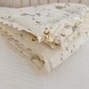 A folded white muslin baby blanket with gold star and crescent moon embroidery resting on a white surface.